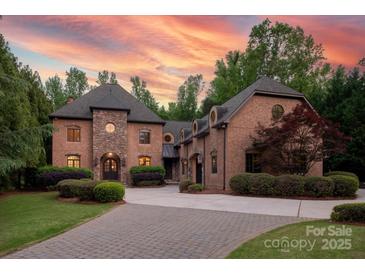 Stunning two-story home with stone accents, lush landscaping, and a paver driveway, set against a vibrant sunset sky at 1504 Alydar Ct, Waxhaw, NC 28173