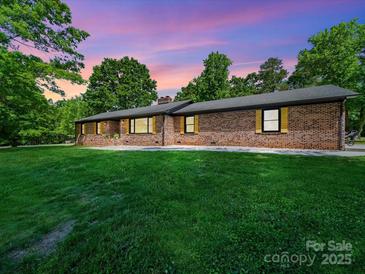 Charming brick home with a spacious front yard and mature trees, set against a beautiful sunset sky at 1207 Carlson Dr, Monroe, NC 28110