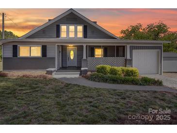 Charming gray home with a cozy front porch and well-manicured landscaping at sunset at 225 N Main St, Mount Pleasant, NC 28124