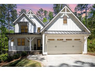 Beautiful two-story farmhouse with white siding, black trim, and a welcoming front porch and attached garage at 16432 Here At Last Ln, Charlotte, NC 28278
