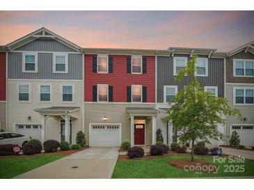 Charming townhome featuring colorful siding, a driveway, manicured lawn, and a covered front porch at 1206 Keydet Dr, Charlotte, NC 28216