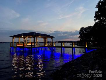 Picturesque waterfront dock featuring a covered boat slip with blue underwater lighting at dusk at 578 Stonemarker Rd, Mooresville, NC 28117