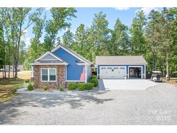 Charming blue home with stone accents, three-car garage and gravel driveway surrounded by lush trees at 720 Cricket Ln, Mt Ulla, NC 28125