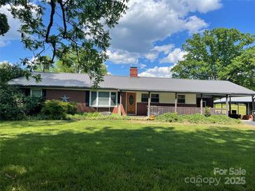 Charming brick home featuring a metal roof, covered front porch, and a spacious green lawn at 180 Needmore Rd, Woodleaf, NC 27054