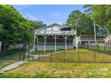 Charming lake house featuring a multi-level deck, lush landscaping, and a secure fenced yard at 592 Shoreline Rd, New London, NC 28127
