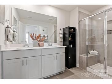 Modern bathroom featuring a double sink vanity, large mirror, black cabinet, and tiled glass door shower at 4229 Summit Woods Dr, Charlotte, NC 28216