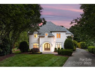 Elegant home featuring an arched entryway, meticulous landscaping, and a gray shingle roof set against a pastel sunset at 15038 Jockeys Ridge Dr, Charlotte, NC 28277
