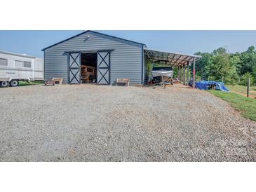 Large metal barn with open sliding doors and covered parking featuring ample gravel space at 2676 Will Schronce Rd, Iron Station, NC 28080