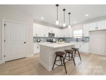 Modern kitchen with white cabinets, stainless steel appliances, and a quartz countertop island with barstool seating at 515 Dixie Dr, Mooresville, NC 28115