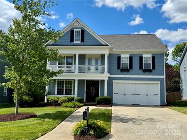 Charming blue two-story home featuring a manicured lawn, a two-car garage and delightful balcony with white railing at 1014 Harrogate Ln, Matthews, NC 28104