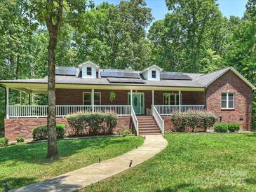 Beautiful brick home featuring a spacious front porch, lush landscaping, and solar panels on the roof at 10545 Mount Holly Huntersville Rd, Huntersville, NC 28078