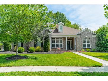 Charming brick home boasts lush lawn, mature trees, and inviting front porch perfect for relaxing at 12039 Lawings Corner Dr, Huntersville, NC 28078