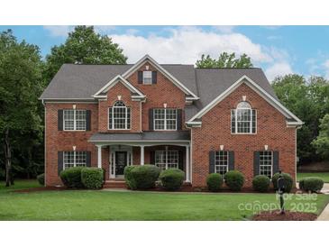 Charming two-story red brick home featuring black shutters, a well-manicured lawn, and lush landscaping at 601 Carver Pond Ln, Waxhaw, NC 28173