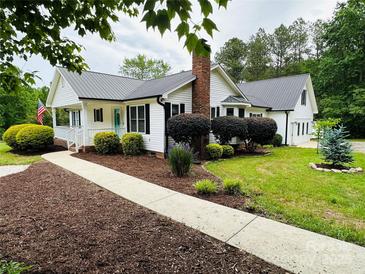 Charming white home featuring a landscaped yard, metal roof and inviting front porch at 120 Mossy Rock Trl, Iron Station, NC 28080