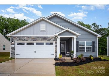 Charming gray home featuring a two-car garage, stone accents, manicured lawn and covered front porch entrance at 107 S Sina St, Troutman, NC 28166