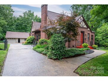 Charming brick Tudor-style home with a red door, lush landscaping, and a detached garage at 1136 S Edgemont Ave, Gastonia, NC 28054