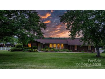 Charming brick home featuring a well-manicured lawn and beautiful landscaping under an orange sunset at 2448 Moss Farm Rd, Hickory, NC 28602