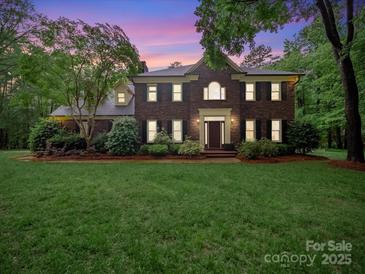 Beautiful brick two-story home with a well-manicured lawn and mature trees during dusk at 8527 Foxbridge Dr, Matthews, NC 28104