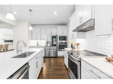 Modern white kitchen features stainless steel appliances, subway tile backsplash, and dark wood flooring at 10901 Greenvale Dr, Harrisburg, NC 28075