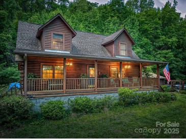 Charming log cabin with inviting covered porch and an American flag, nestled in a lush green setting at 95 Odell Ct, Taylorsville, NC 28681