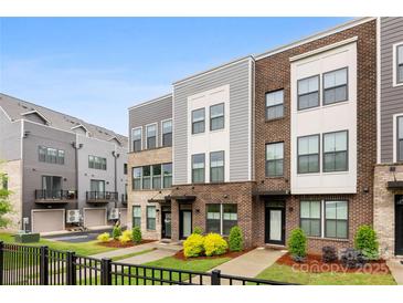 View of new townhomes with a combination of brick and gray siding, well-manicured lawns, and a black fence at 3748 Ellington St, Charlotte, NC 28211