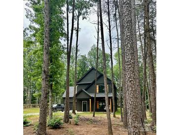 Modern farmhouse with dark siding nestled in trees, featuring a garage and natural wood porch columns at 3020 Quiet Ln, Iron Station, NC 28080