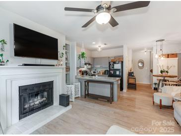 Cozy living room featuring a fireplace, TV, ceiling fan and an open layout to a modern kitchen with an island at 3308 Selwyn Farms Ln # 2, Charlotte, NC 28209