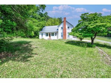 Charming two-story home featuring a brick chimney, metal roof, and lush green lawn with mature trees at 5604 Nc 152 E Hwy, Rockwell, NC 28138