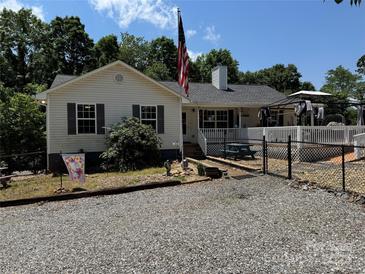 Charming home featuring a well-maintained yard, gravel driveway, and a welcoming front porch with an American flag at 533 Tuckers Grove Rd, Statesville, NC 28625