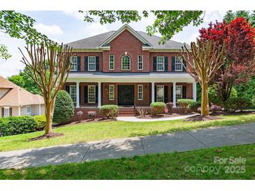 Traditional two-story red brick home with a covered front porch, black shutters, and manicured landscaping at 1009 Brookline Dr, Huntersville, NC 28078
