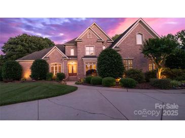 Striking brick home with manicured lawn and circular driveway, illuminated by warm lighting against a vibrant twilight sky at 1509 Churchill Downs Dr, Waxhaw, NC 28173