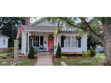 Charming cottage-style home with a welcoming porch, beautiful plants, and mature trees at 105 N Central Ave, Belmont, NC 28012