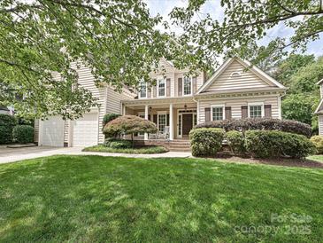 Inviting two-story home with lush landscaping, a front porch with rocking chairs, and attached two car garage at 2406 Tarleton Twins Ter, Charlotte, NC 28270