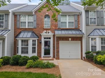 Charming brick townhouse featuring a one-car garage, black awnings, lush landscaping, and a welcoming entrance at 1647 Backcreek Ln, Gastonia, NC 28054