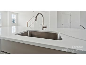 New construction home boasts a kitchen island with a stainless steel sink and modern faucet at 9214 Delancey Ln # 62, Concord, NC 28027