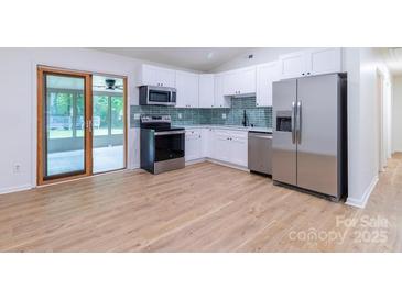 Bright kitchen features stainless steel appliances, white cabinetry, and adjacent sunroom at 5233 Great Wagon Rd, Charlotte, NC 28215