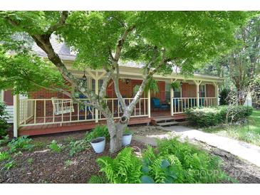 Inviting brick home featuring a charming front porch, mature tree, and lush landscaping at 109 Larch Rd, Salisbury, NC 28147