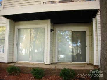 A condo's back patio with two sliding glass doors and a small brick patio lined with greenery at 9603 Vinca Cir # A, Charlotte, NC 28213