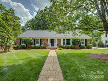 Charming brick home featuring a manicured lawn, mature landscaping, and welcoming walkway to the front door at 6116 Springhouse Ln, Charlotte, NC 28211