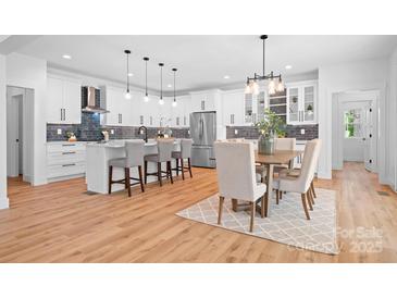Modern kitchen with white cabinetry, stainless steel appliances, a kitchen island, and an adjacent dining area at 106 Arbor Dr, Waxhaw, NC 28173