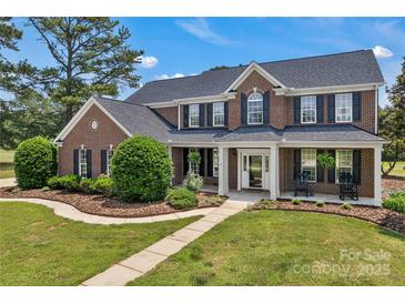 Charming two-story brick home featuring a manicured lawn, lush landscaping, and inviting front porch with rocking chairs at 3068 River Rd, Shelby, NC 28152