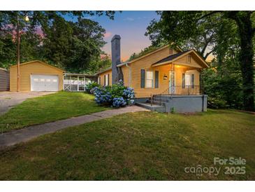 Charming yellow home featuring a detached garage, blooming hydrangeas, and inviting front porch at 310 S Spencer Ave, Spencer, NC 28159