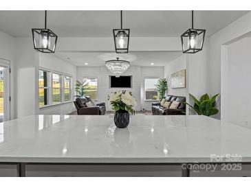Modern open-concept design showcasing the kitchen island with quartz countertops and pendant lighting overlooking the living room at 3127 Pinehills Way, Mount Holly, NC 28120
