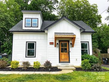 Charming home featuring white vertical siding, a covered wood porch, black trim, and landscaped yard at 125 Todd Nw Dr, Concord, NC 28025