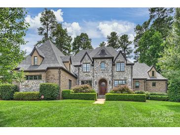 Stunning stone-clad home featuring a manicured lawn and lush, mature landscaping at 3032 Kings Manor Dr, Matthews, NC 28104
