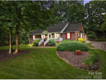 Charming brick home featuring a welcoming front porch, lush landscaping, and mature trees at 635 Timberlane Trl, Salisbury, NC 28147