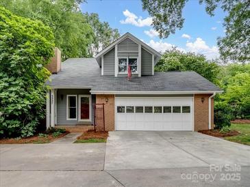 Charming home with a two-car garage and dormer, set amidst lush greenery, features a gray facade and brick accents at 3327 Archdale Dr, Charlotte, NC 28210