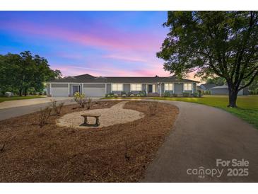 Charming single-story home with manicured front yard and three-car garage, lit by dusk sky at 15020 Ranson Rd, Huntersville, NC 28078