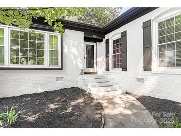 Charming home features a white brick facade, black trim, and lush landscaping for appealing curb appeal at 6128 Coatbridge Ln, Charlotte, NC 28212
