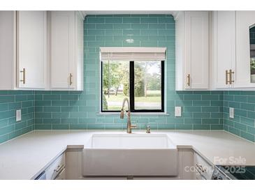Bright kitchen features a farmhouse sink, white cabinets, a window, and stylish turquoise backsplash at 712 Mallard Head Ln, Mooresville, NC 28117